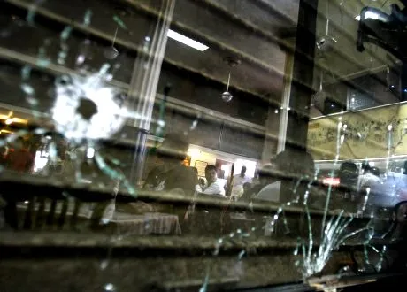 People are reflected in a mirror with bullet holes at Cafe Leopold, one of the several places where terrorists shot at people, after it reopened in Mumbai, India, Monday, Dec. 1, 2008. (AP Photo/Altaf Qadri)